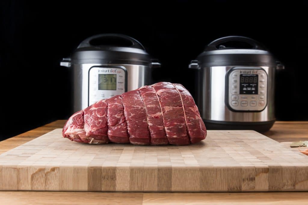 uncooked beef roast on a cutting board with two electric pressure cookers behind it