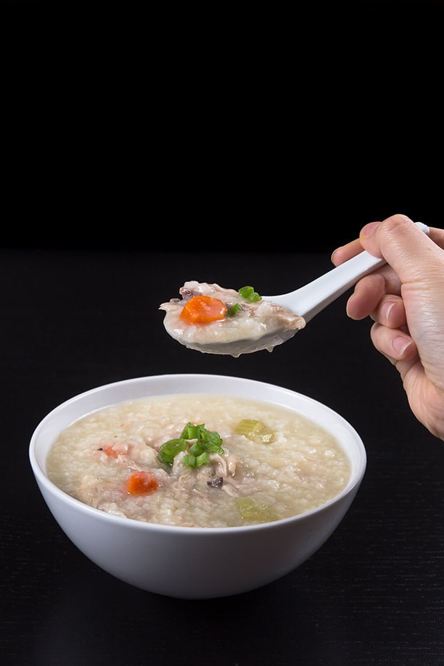 bowl of Pressure Cooker Turkey Rice Porridge with someone holding a big spoonful of porridge above it