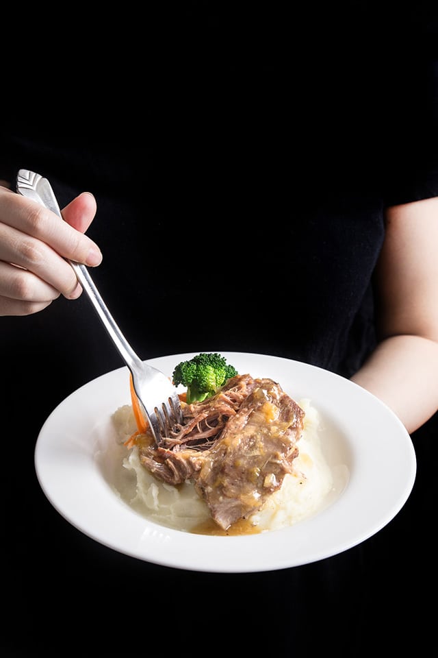 someone holding a white dinner plate with shredded Asian pork. A fork is in the right hand.