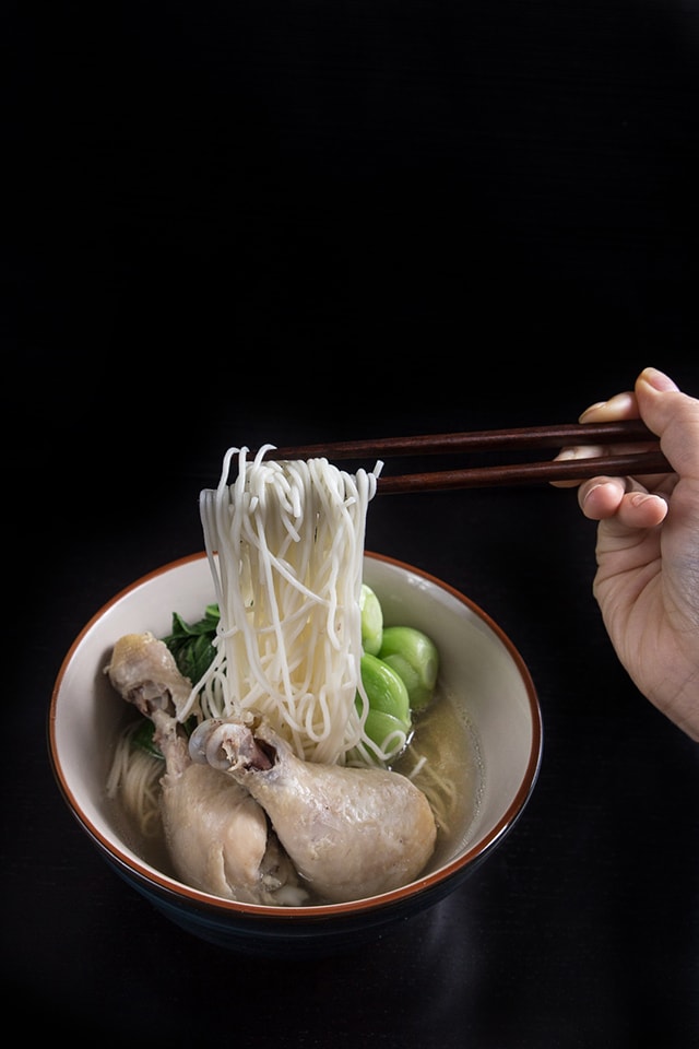 Asian Bok Choy Chicken Noodle Soup in a bowl. Pressure cooked noodles being held with chopsticks