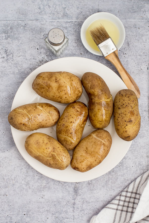 white plate of large baking potatoes brushed with olive oil for roasting or crisping in a pressure cookier