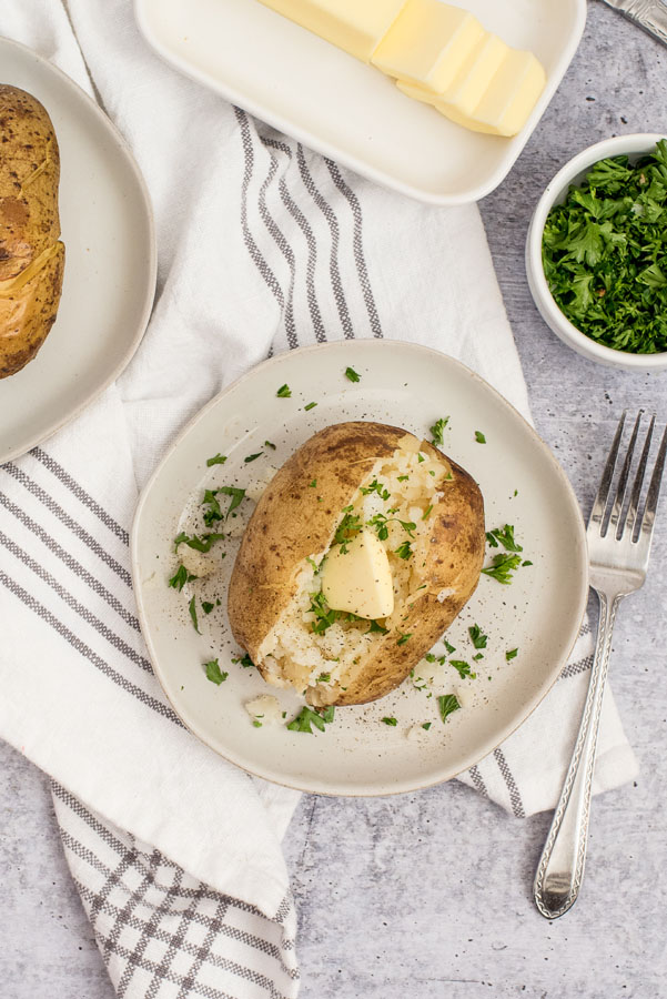 pinterest button with instant pot baked potatoes topped with butter and minced fresh herbs on a white plate