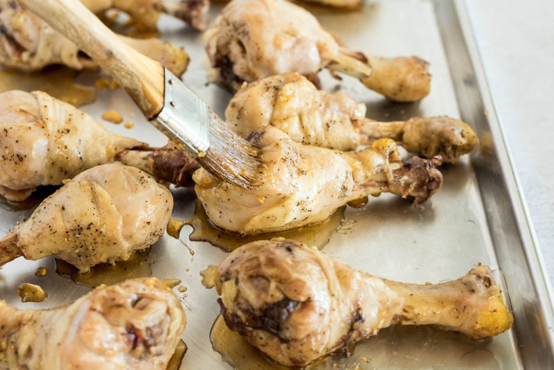 Basting cooked chicken drum sticks with honey sriracha sauce, preparing to finish them on the grill.