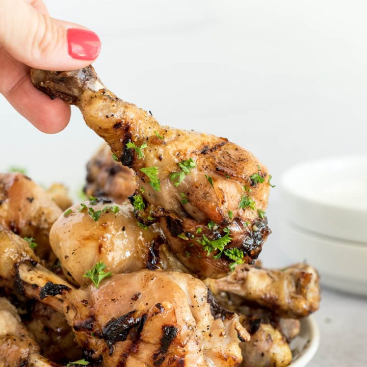 A hand grabbing a drumstick from a plate of honey Sriracha chicken drumsticks cooked in an Instant Pot.