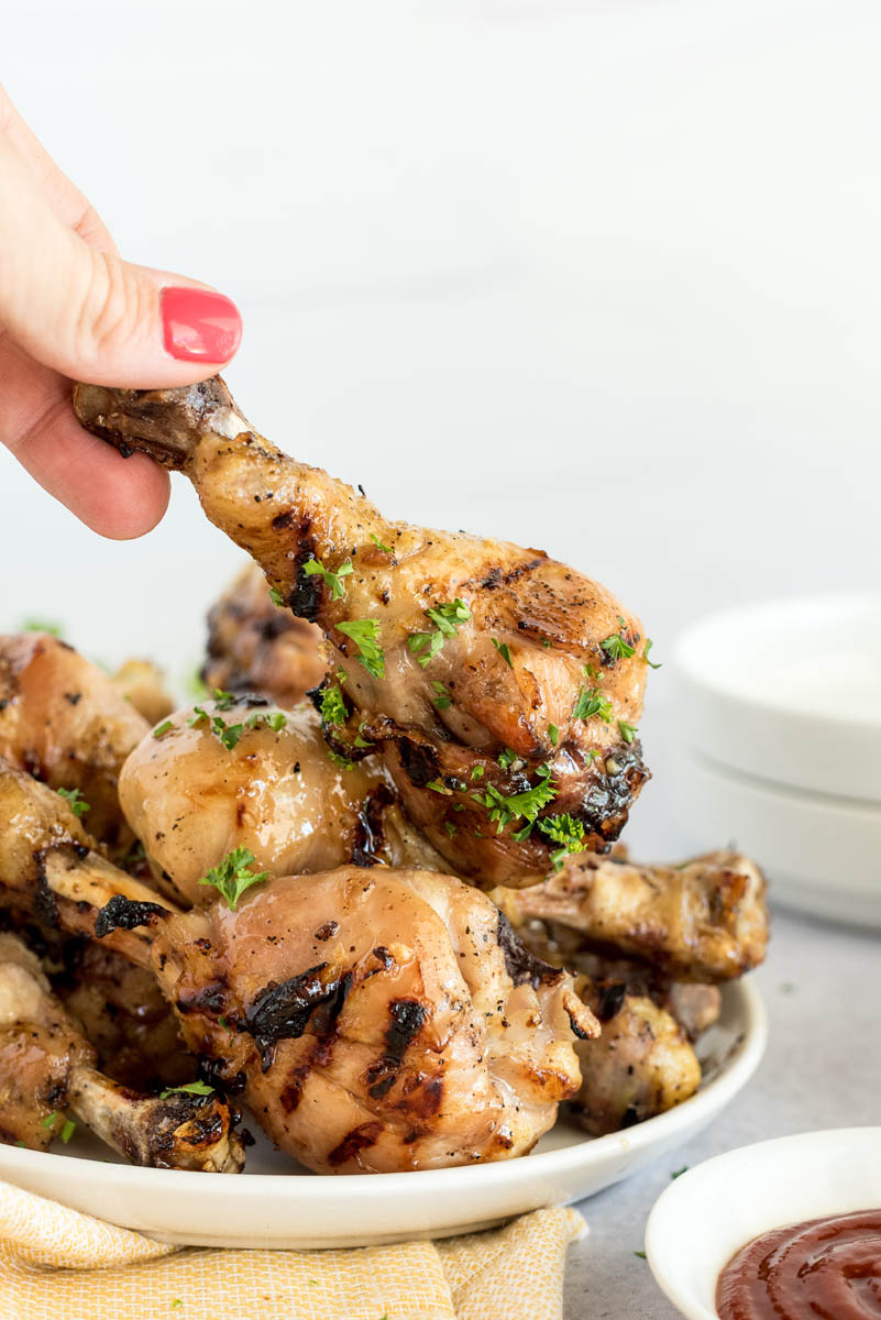 A hand grabbing a drumstick from a plate of honey Sriracha chicken drumsticks cooked in an Instant Pot.