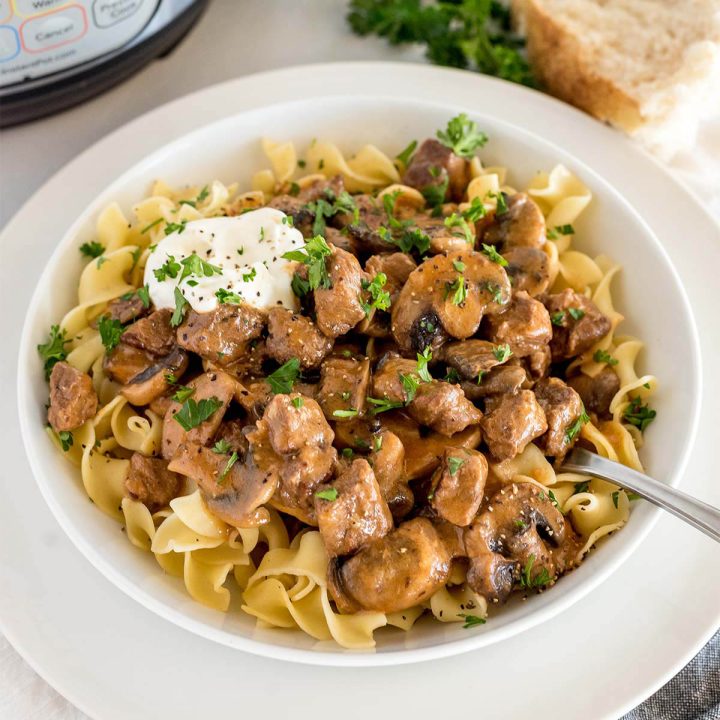 a square photo of instapot beef stroganoff garnished with parsley and sour cream