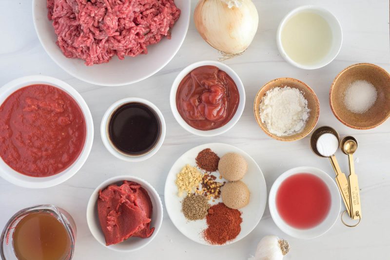 An overhead shot including all the ingredients for Instant Pot Sloppy Joes, including ground beef, spices, tomato paste, crushed tomatoes, beef broth, ketchup, onion, and red wine vinegar.