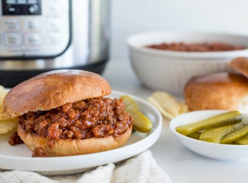 Sloppy Joe served on a bun with pickles, rolls, sloppy box mix, and an Instant Pot in the background.