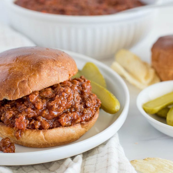 Instant Pot Sloppy Joe served on a bun with pickles and sloppy Joe mix in the background.