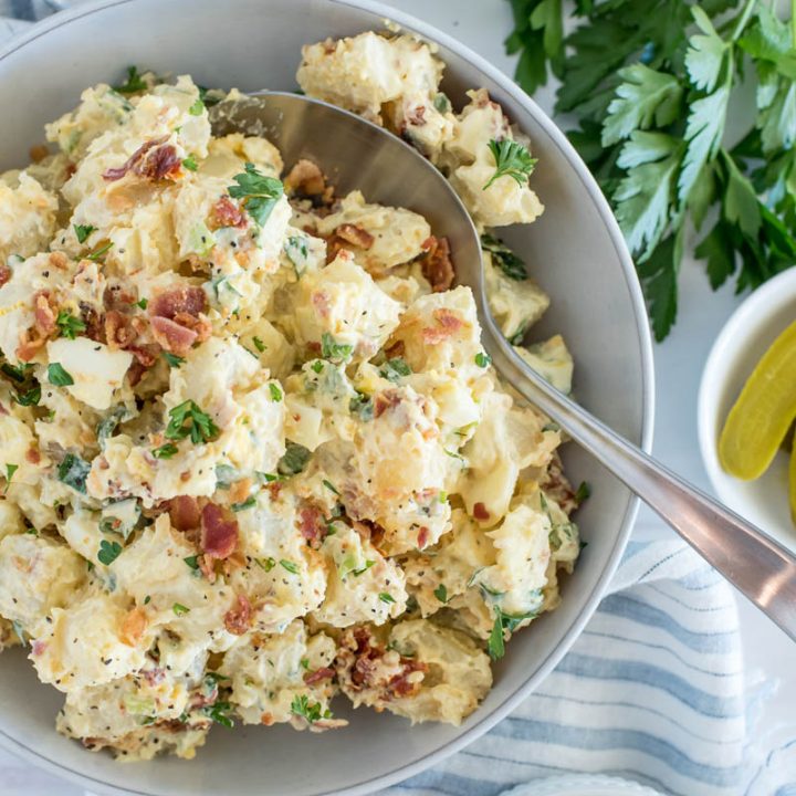 Overhead picture of Instant Pot potato salad with bacon and tomatoes added, with parsley and pickles in the background.