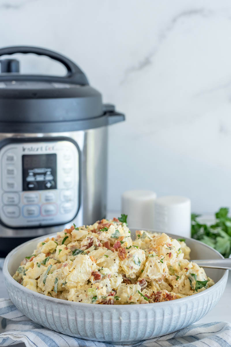 Bowl of BLT potato salad placed in front of an Instant Pot, with parsley and salt and pepper shakers in the background.