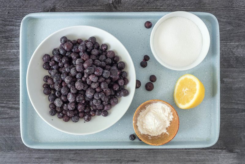 A picture of ingredients for Instant Pot blueberry compote, including frozen blueberries, sugar, fresh lemon, and cornstarch.
