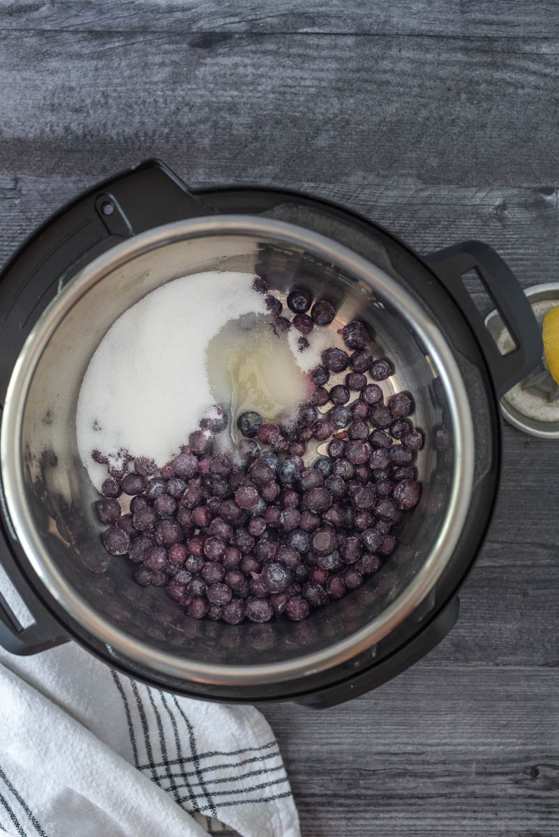 Overhead picture of an Instant Pot with frozen blueberries, sugar, and lemon juice inside for making blueberry compote.