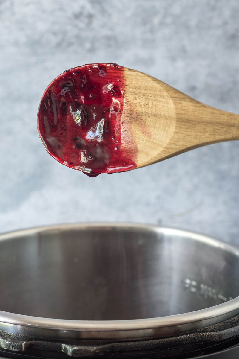 A wooden spoon used to stir blueberry compote in an Instant Pot.