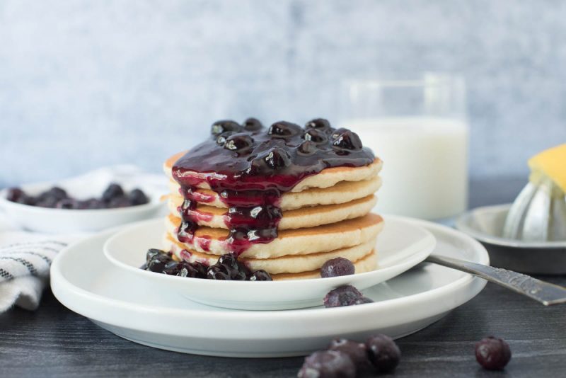 A stack of pancakes on a white plate topped with Instant Pot blueberry compote.