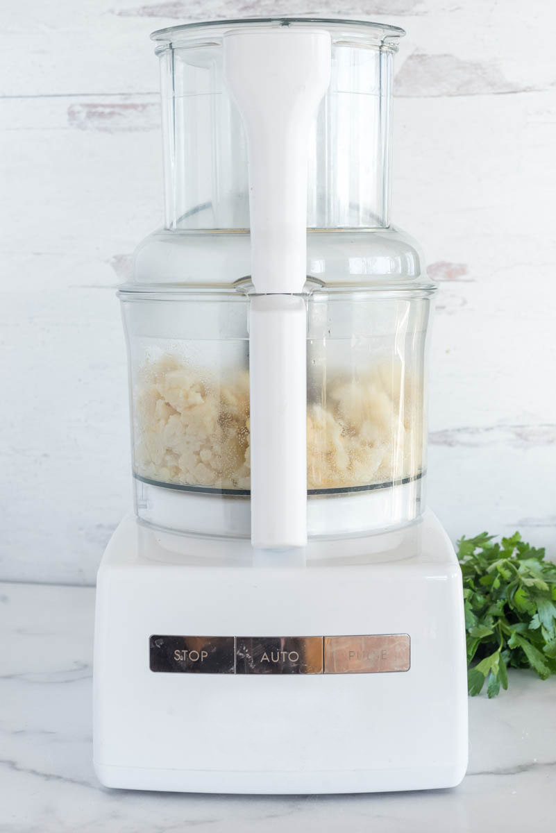 A direct shot of a food processor, filled with the cooked cauliflower