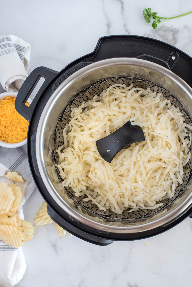 A steamer basket with hash brown in an Instant Pot for making hash brown casserole.