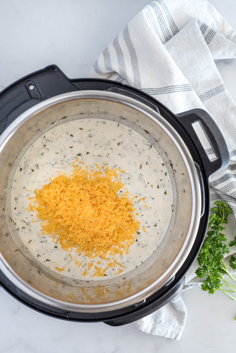 Adding cheese to the hash brown casserole inside an Instant Pot.