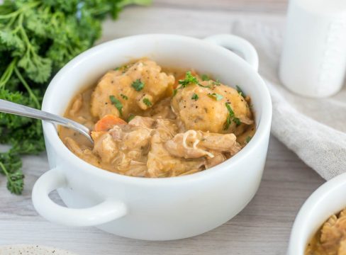 Close up picture of a white bowl with Instant Pot chicken and dumplings, with fresh parsley and another bowl of chicken and dumplings in the background.