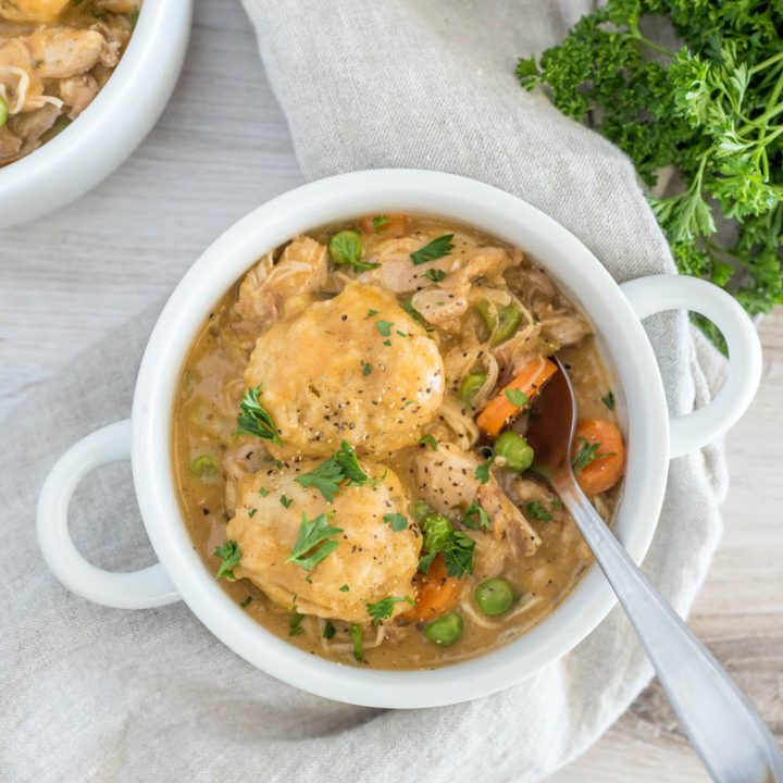 Overhead picture of a white bowl with Instant Pot chicken and dumplings with fresh chopped parsley on a plate in the background.