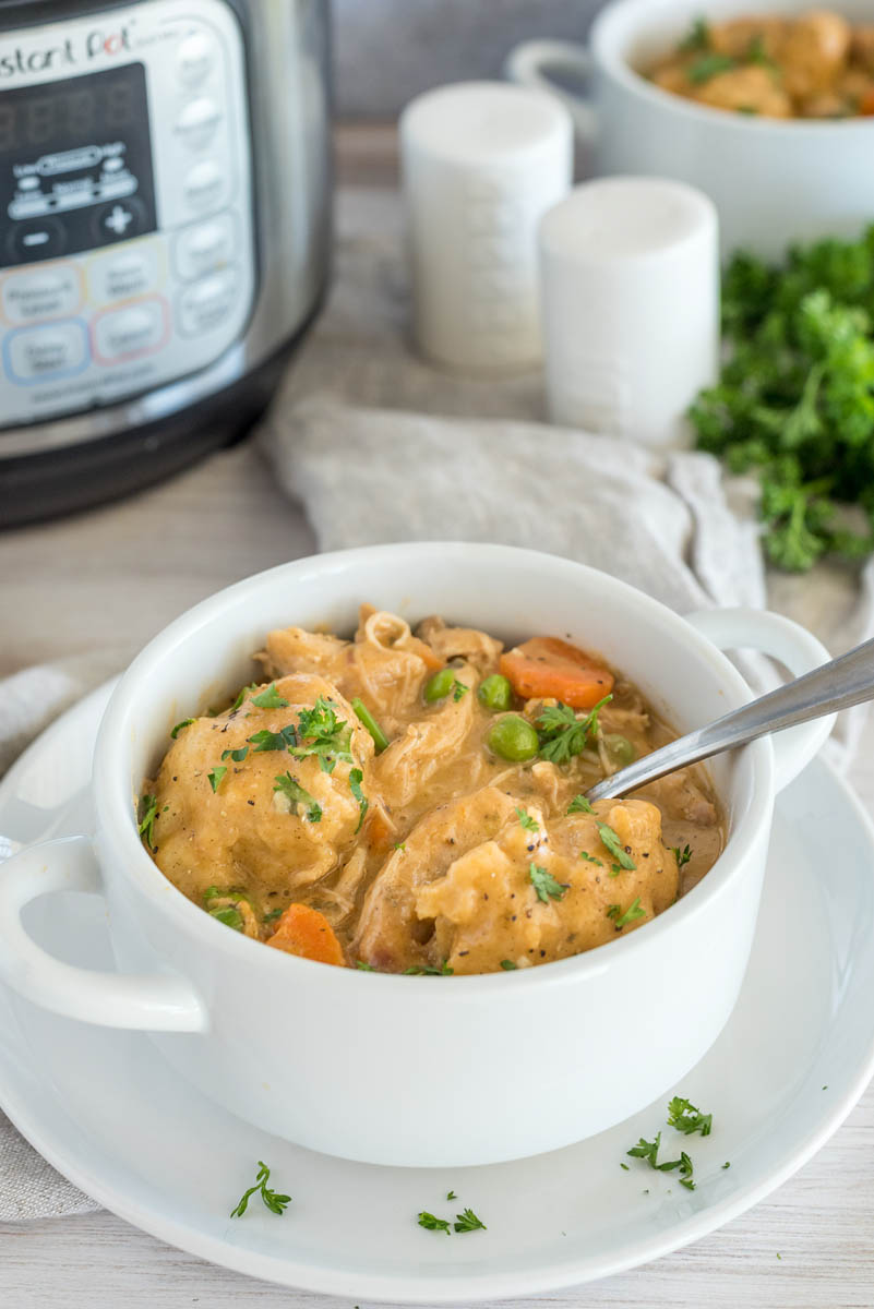 Chicken and dumplings ready to serve in a white bowl, with fresh parsley and an Instant Pot in the background