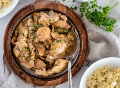 an overhead shot looking into a dark bowl on a wooden platter, filled with cooked chicken marsala ready to spoon onto pasta