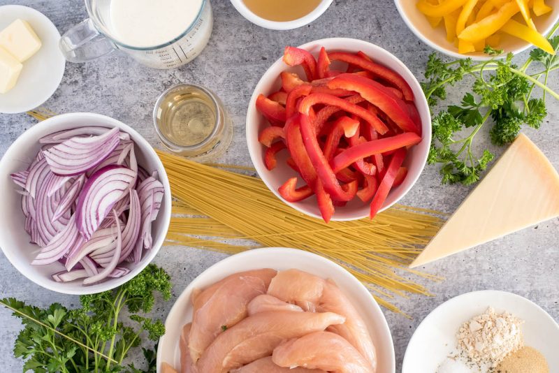 an overhead shot of the ingredients needed for Chicken Scampi, including red onions, chicken tenders, bell peppers, cream, butter, parmesan, and spices
