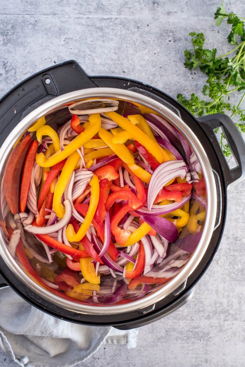 An overhead shot of an Instant Pot filled with bright red bell peppers, yellow peppers, and red onions sliced in thin long strips