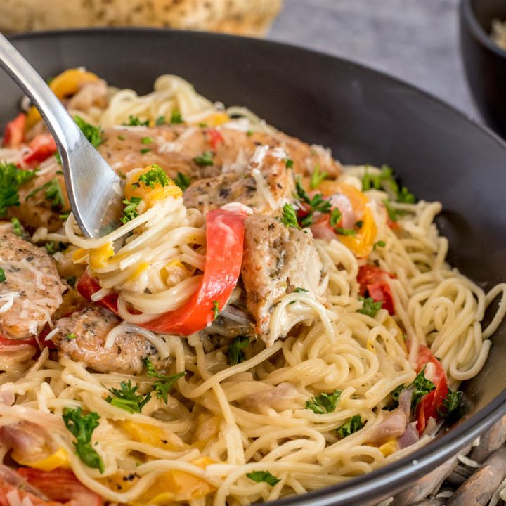A fork with a twist of pasta noodles, with bell pepper and chicken ready to scoop into a bite