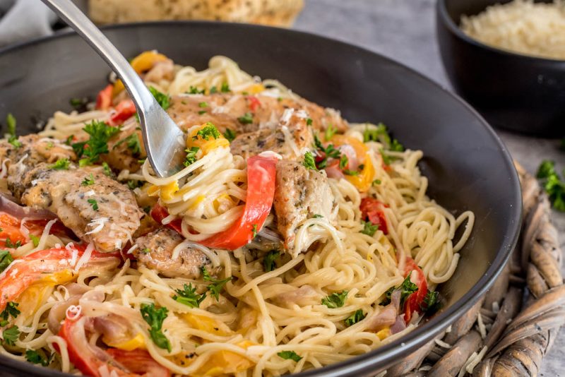 A fork with a twist of pasta noodles, with bell pepper and chicken ready to scoop into a bite