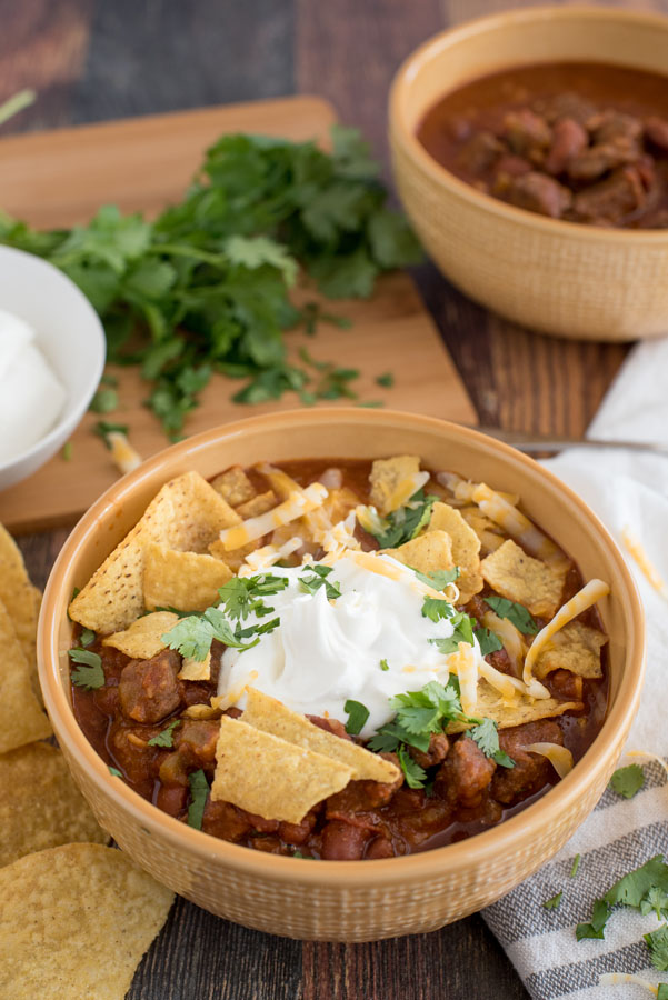 A yellow bowl of Easy Pressure Cooker Chili, topped with sour cream, cheese, cilantro, and tortilla chips