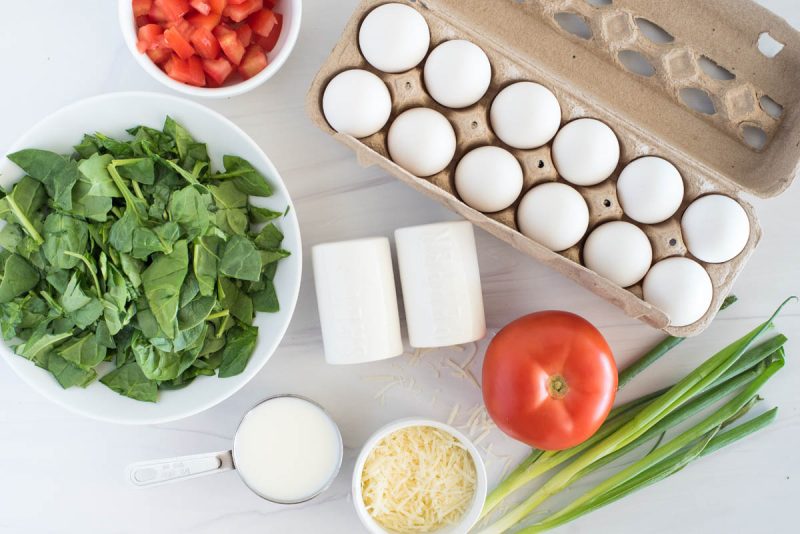 Ingredients for an Instant Pot crustless spinach quiche, including spinach, eggs, green onion, cheese, flour, and tomatoes.