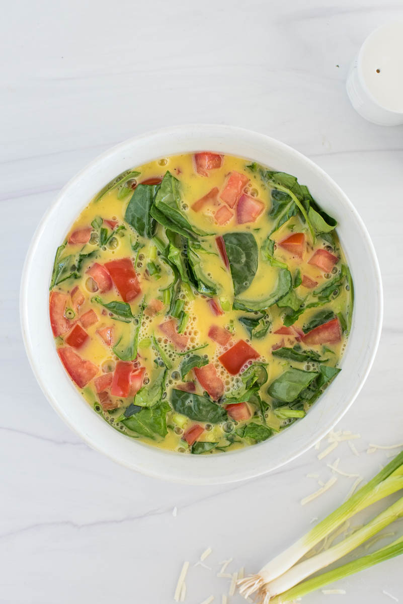 Mixed eggs in a white bowl mixed with diced tomatoes and spinach for an Instant Pot crustless spinach quiche
