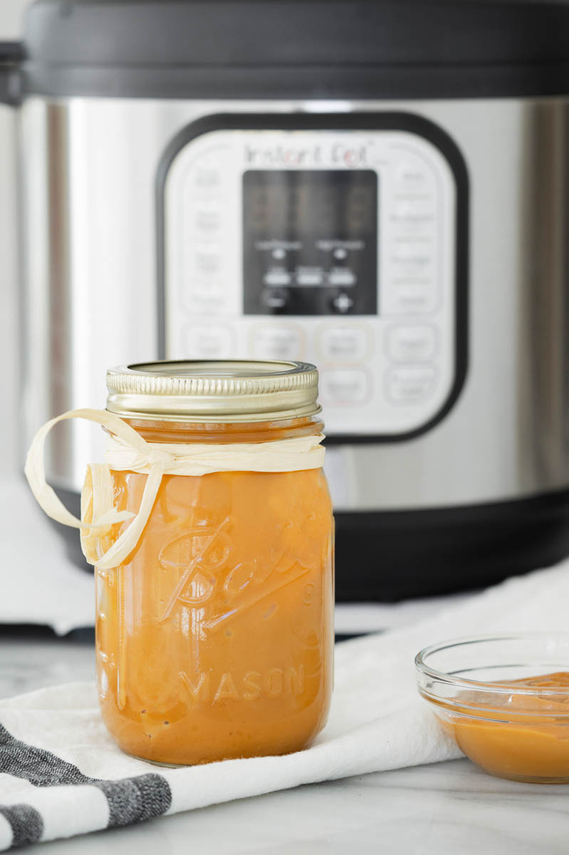 A mason jar with dulce de leche and a ribbon tied around the mason jar, placed in front of an Instant Pot.