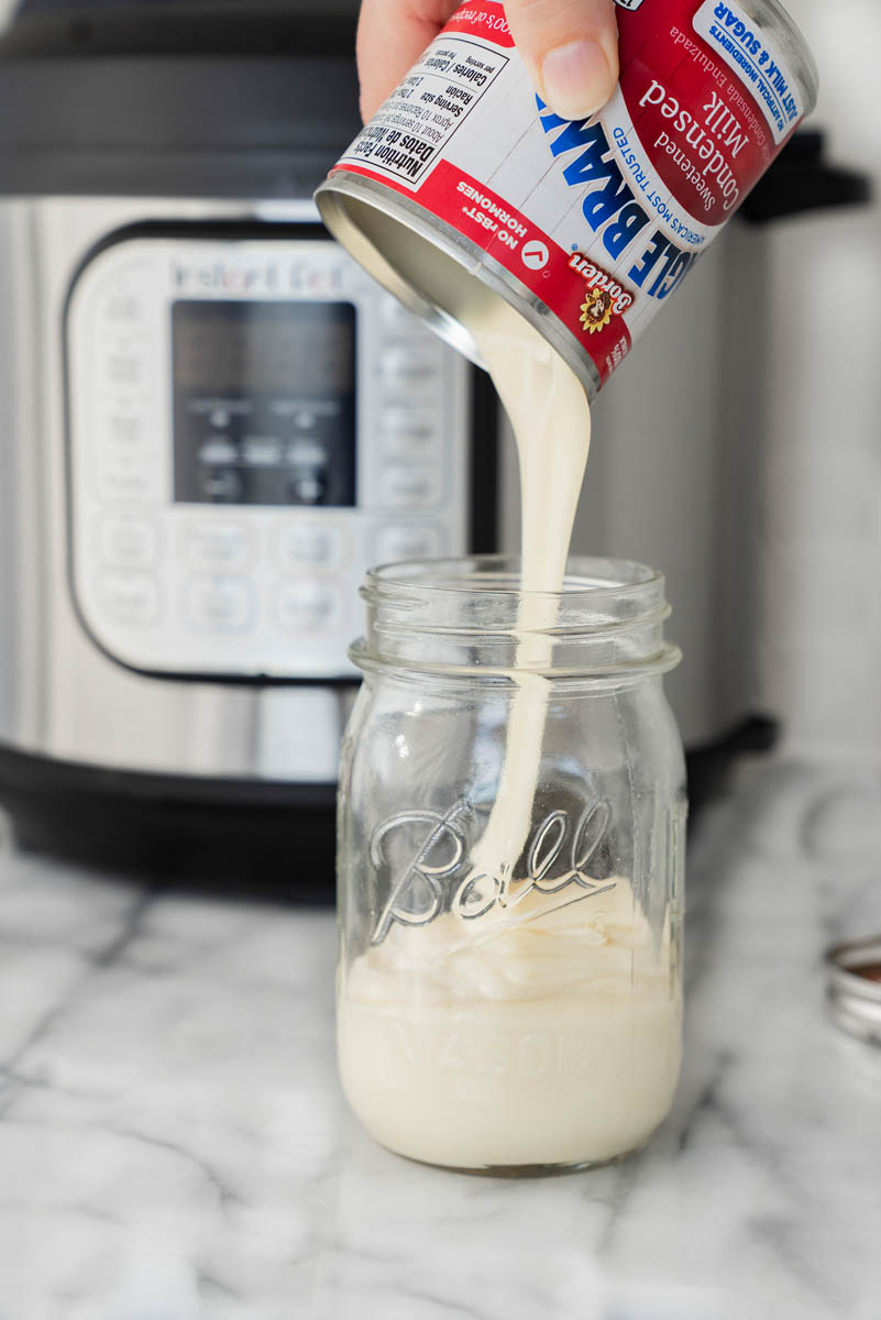 Pouring a can of sweet and condensed milk into a mason jar and placed in front of an Instant Pot for making dulce de leche