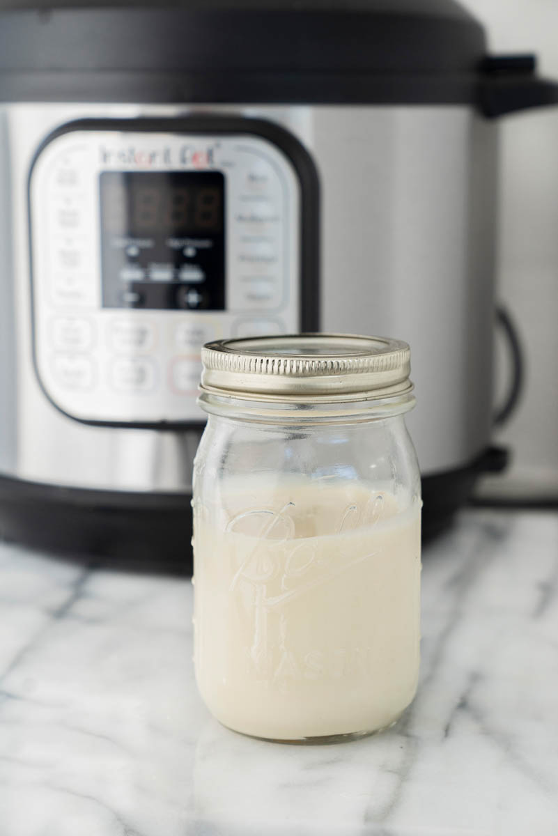 A mason jar with sweet and condensed milk placed in front of an Instant Pot for making dulce de leche