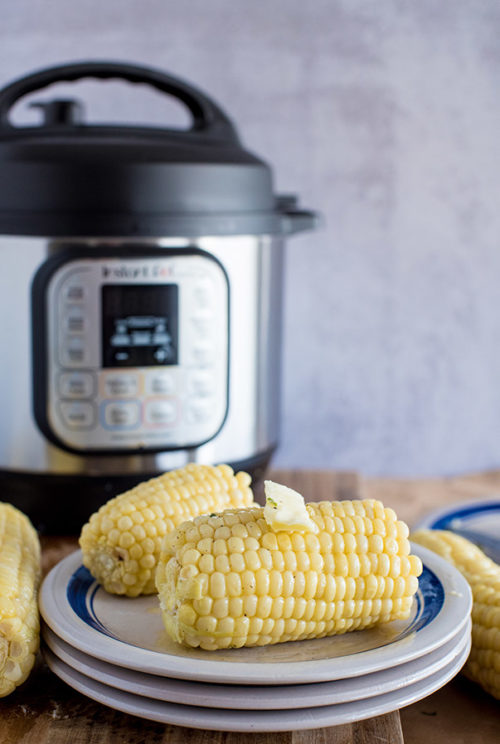 Corn on the Cob, plated and drizzled in butter, with an Instant Pot in the background