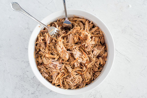 White bowl showing how to shred easy Instant Pot Pulled Pork with two forks