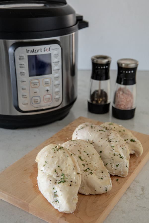 Instant Pot Pressure Cooker Frozen Chicken Breasts on a cutting board with Instant Pot and salt and pepper in the background.
