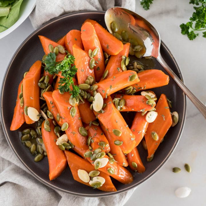 A small dark brown rimmed plate filled with Instant Pot glazed carrots, with pepitas and pumpkin seeds and garnished with parsley