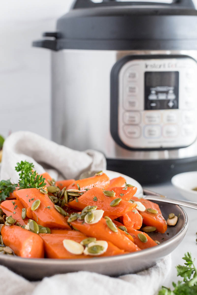 A straight-on shot of glazed carrots on a gray rimmed plate with an Instant Pot visible in the background