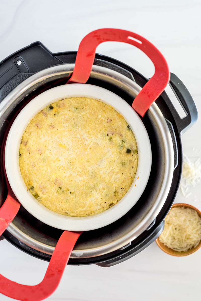 an overhead shot of the egg and ham mixture mixed in with the soufflé pan lowered into the Instant Pot on a red trivet