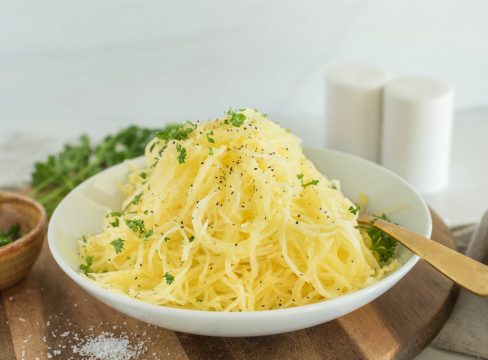 a horizontal shot of a bowl of spaghetti squash, garnished with parsley and sprinkled with salt and peper