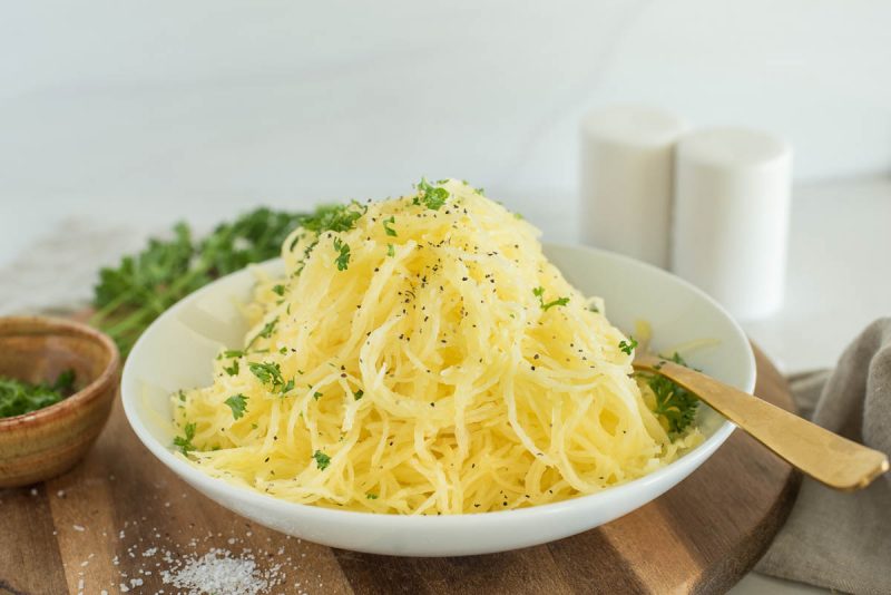 a horizontal shot of a bowl of spaghetti squash, garnished with parsley and sprinkled with salt and peper