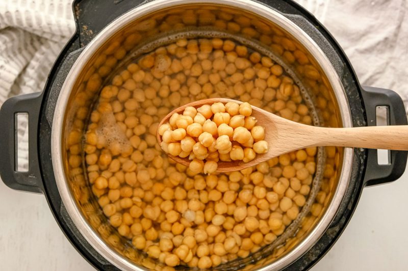 spoon holding cooked chickpeas over an instant pot