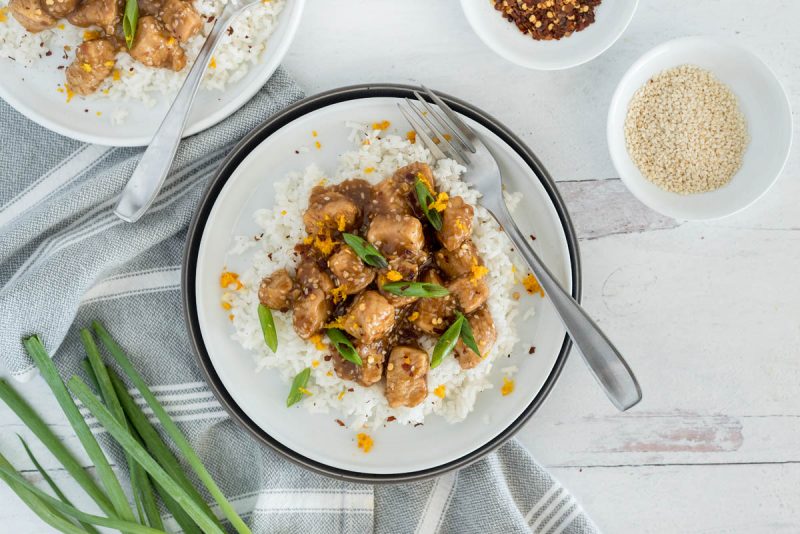 An overhead shot of Instant Pot Teriyaki Chicken, served with a fork and sesame seeds and red pepper flakes and green onions on the edges of the photo