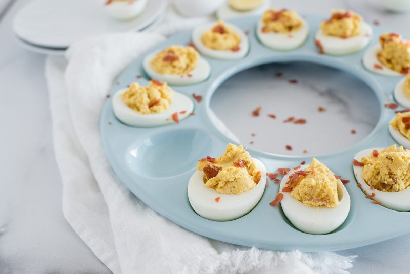 45 degree overhead of a blue circular egg tray filled with Instant Pot BBQ deviled Eggs with crumbled bacon with one egg removed.