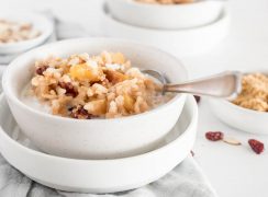 a white bowl of Instant Pot Apple Risotto with Cherries and diced apples, with a silver spoon sticking out the side and topped with additional milk