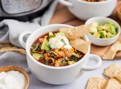 Close up picture of chicken enchilada soup topped with cheese, avocado, sour cream and chips. Placed in front of an Instant Pot.