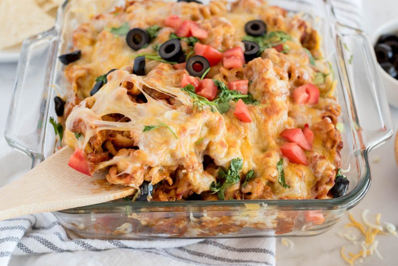 Instant Pot chicken enchilada pasta being scooped from a serving dish using a wooden spoon.